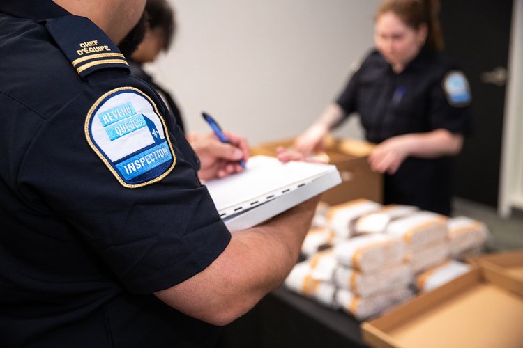 Tabac - 16 - <p>Inspecteurs consignant dans un document les articles saisis, dont des cigarettes de contrebande</p>